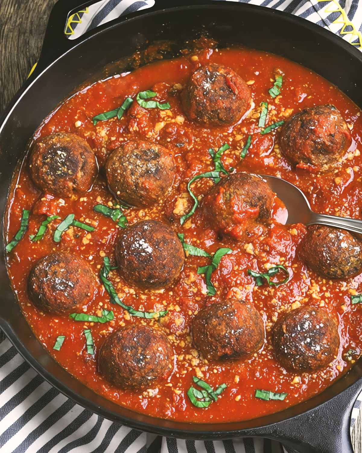 A skillet of tender ultimate vegan meatballs simmering in rich tomato sauce and garnished with fresh basil, perfect for vegan Thanksgiving appetizers.