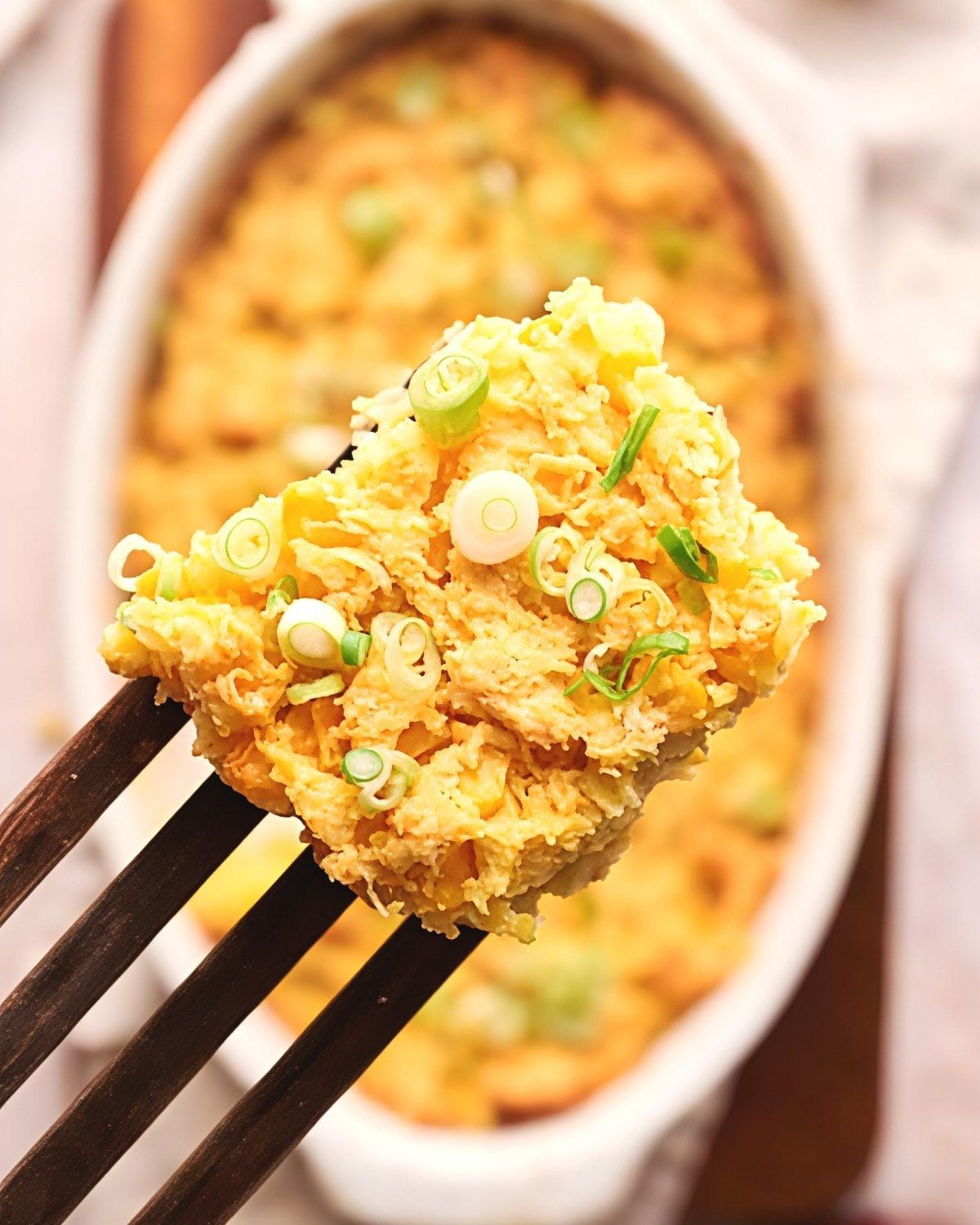 Creamy vegan corn casserole held on a fork, garnished with green onions, as a delicious Thanksgiving side dish.