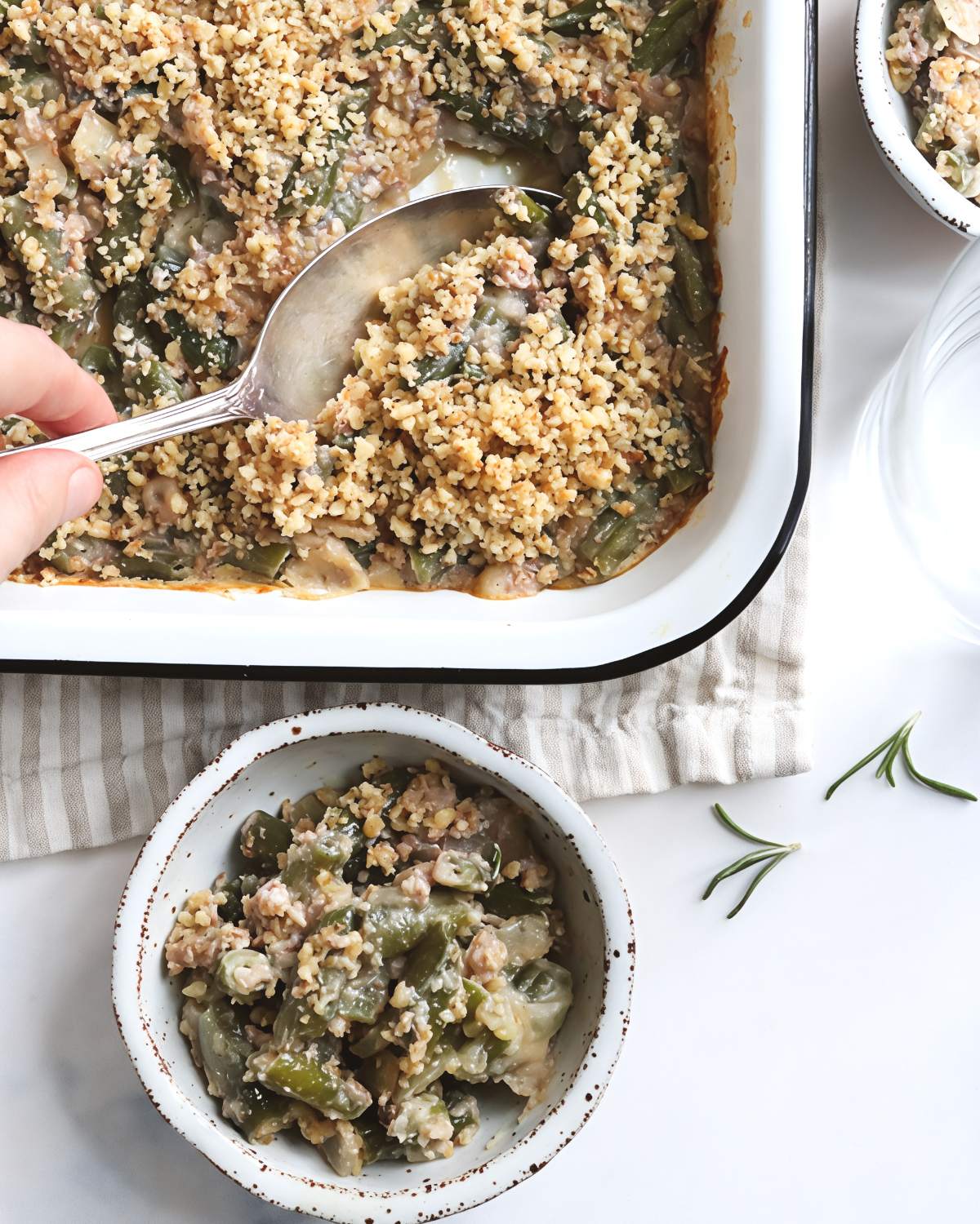 Homemade green bean casserole in a white enamel baking dish with a creamy mushroom sauce and a crunchy panko topping, perfect for a vegan Thanksgiving side dish.