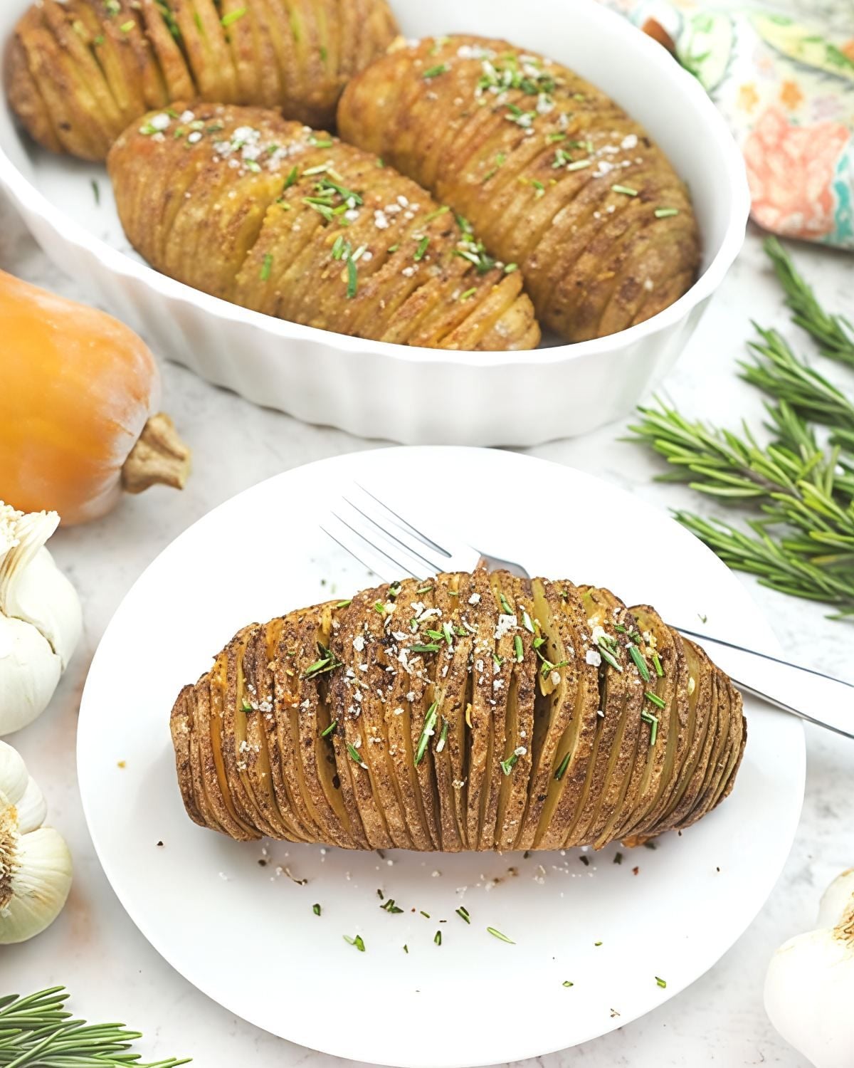 Crispy vegan hasselback potatoes seasoned with rosemary, sea salt, and herbs served on a white plate as a Thanksgiving side dish.