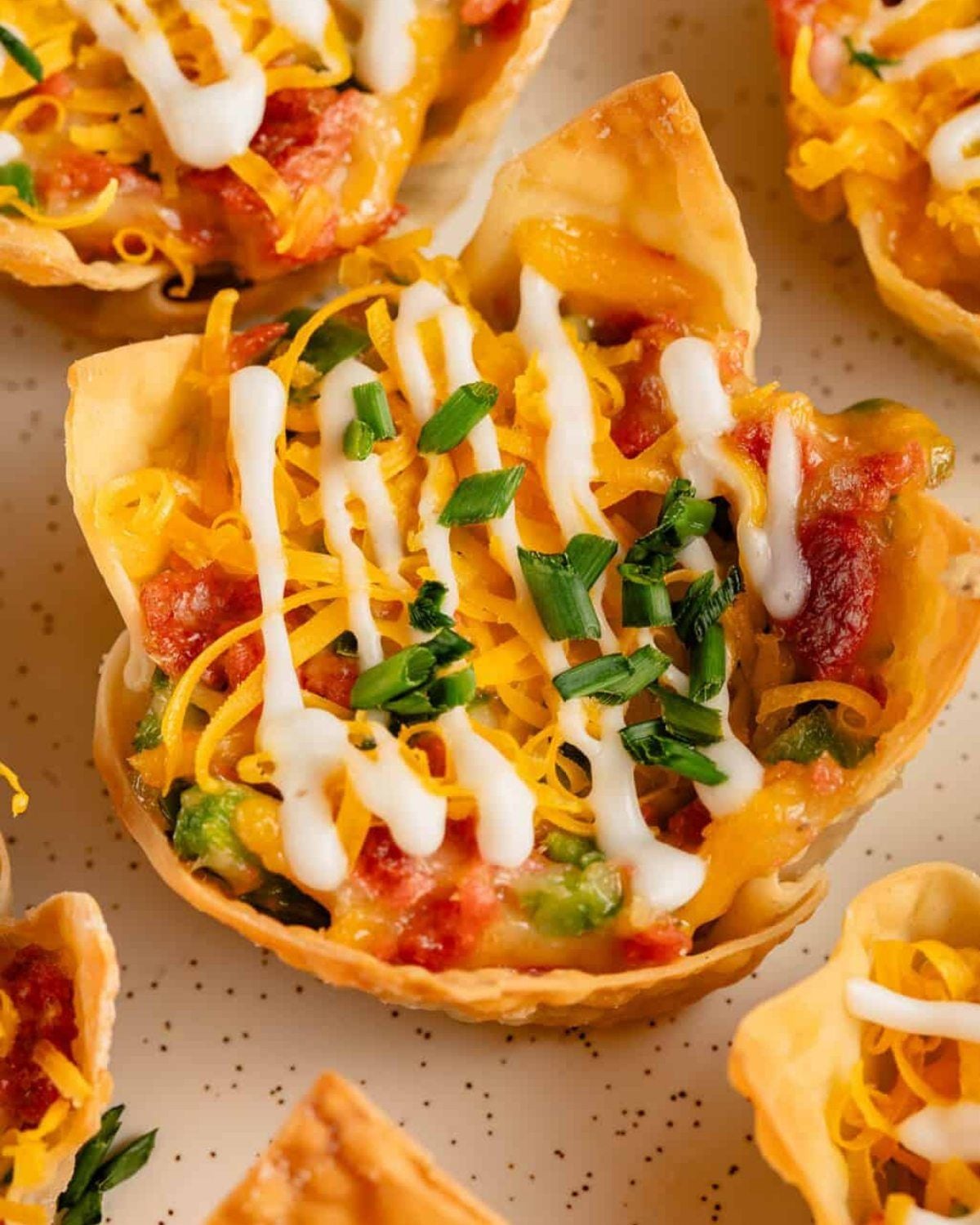 Crispy vegan jalapeรฑo popper wonton cups melted with shredded cheese, drizzled with white cream, and topped with fresh chives, served as delicious vegan Thanksgiving appetizers.