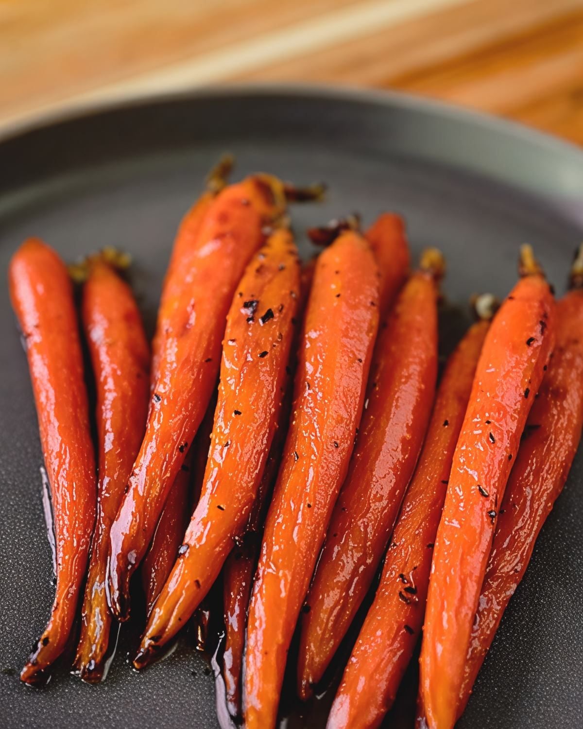 Vegan maple glazed carrots roasted to perfection on a dark plate, serving as a sweet and savory Thanksgiving side dish.