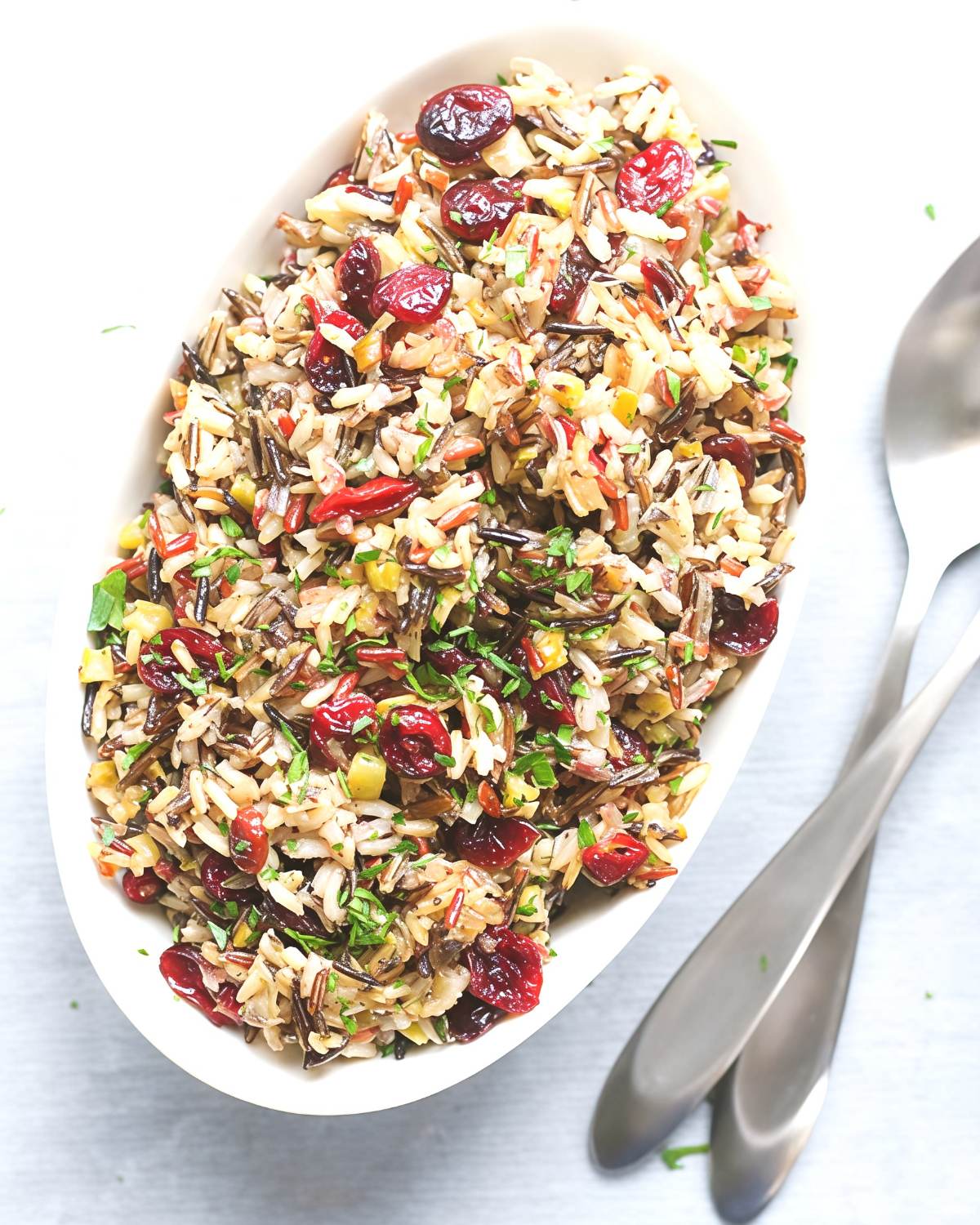 Vegan wild rice stuffing with cranberries in an oval white serving dish, perfect for a festive Thanksgiving side dish.