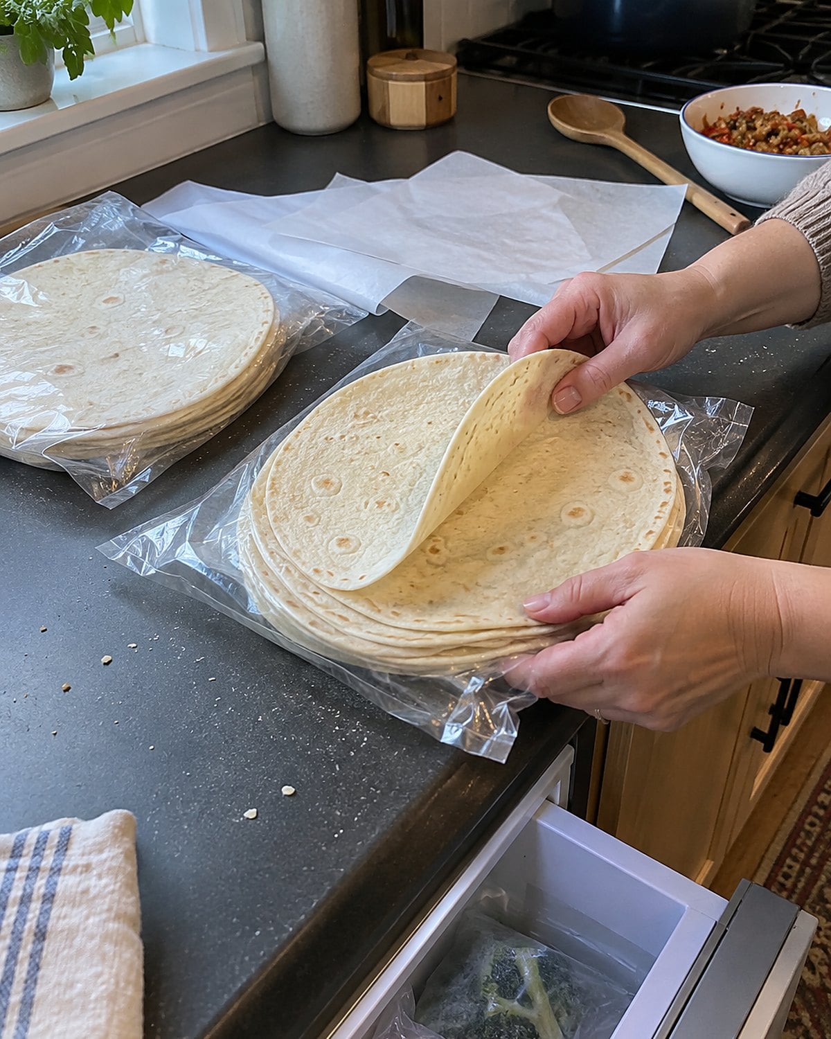 Two packs of flour tortillas beside parchment sheets and an open freezer drawer.