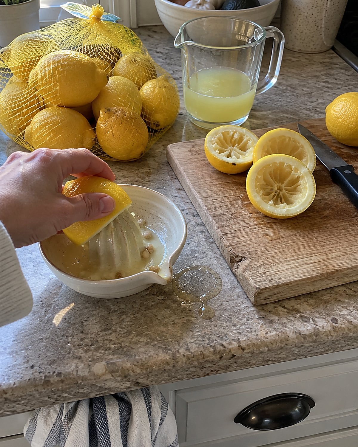 A sack of lemons on a counter beside a cut lemon and a hand juicer.
