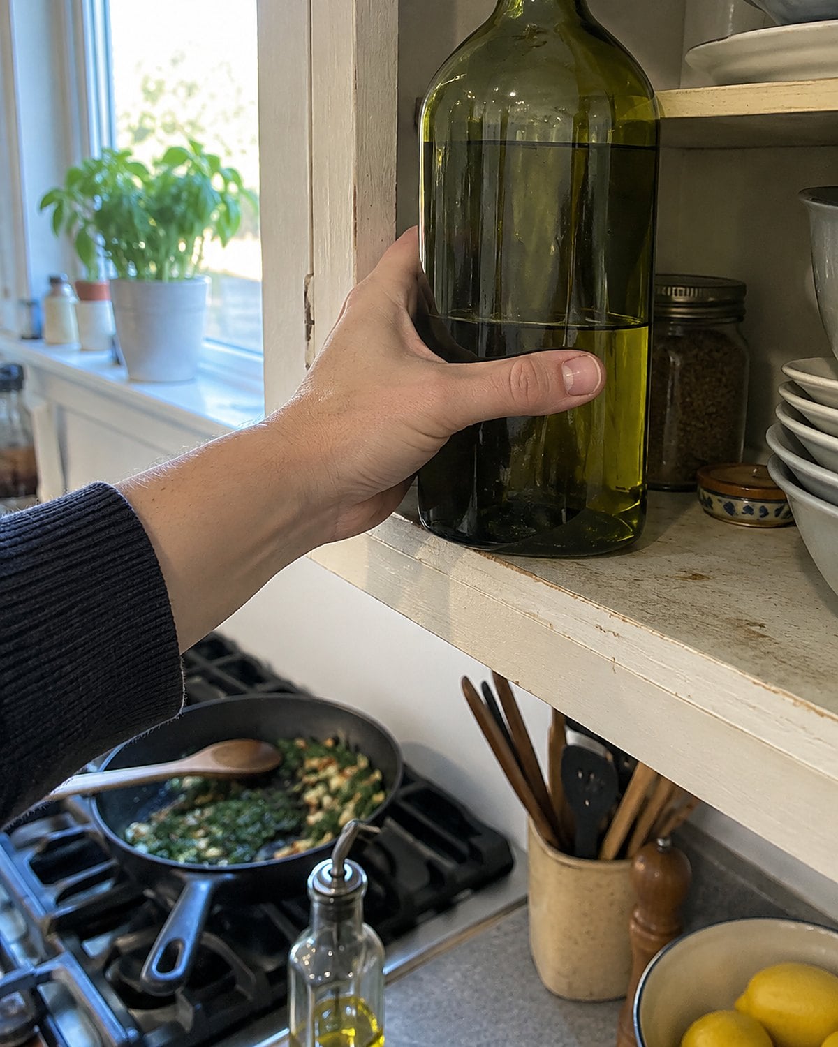 A large olive oil bottle on a cabinet shelf, with a small pourer near the stove.
