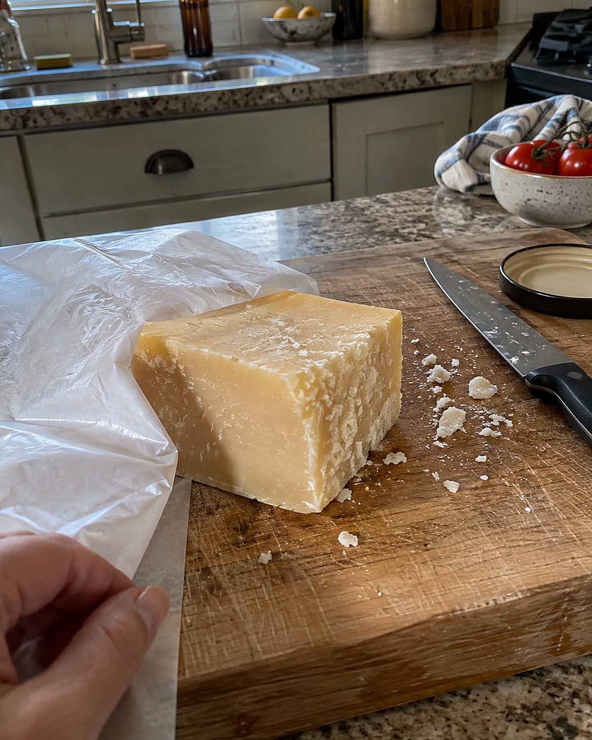 A block of cheese with a dry cut edge on a board beside fresh wrapping.