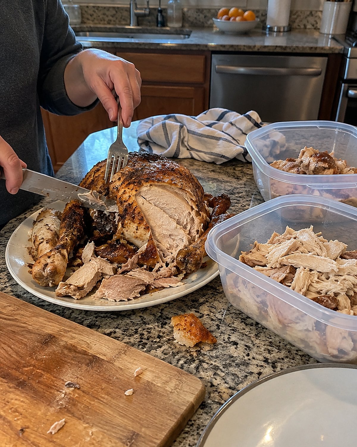 A partly carved rotisserie chicken beside shallow storage containers on a kitchen counter.